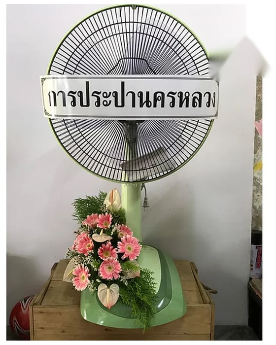 พัดลมสีเขียวอ่อน ช่อเยอบีร่าชมพูทรงสูงข้างฐาน แซมหน้าวัวขาวอมชมพูและใบฝอยสีเขียว