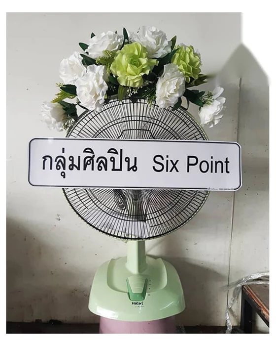 ช่อกุหลาบขาวแซมดอกสีเขียวอ่อนและใบเขียวโค้งตามขอบบนตะแกรงพัดลมสีเขียวอ่อน