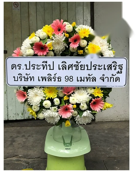 พวงหรีดพัดลมมีวงดอกเยอบีร่าชมพู เบญจมาศขาวและเหลืองล้อมหน้าพัดลม ตั้งบนฐานสีเขียวอ่อน